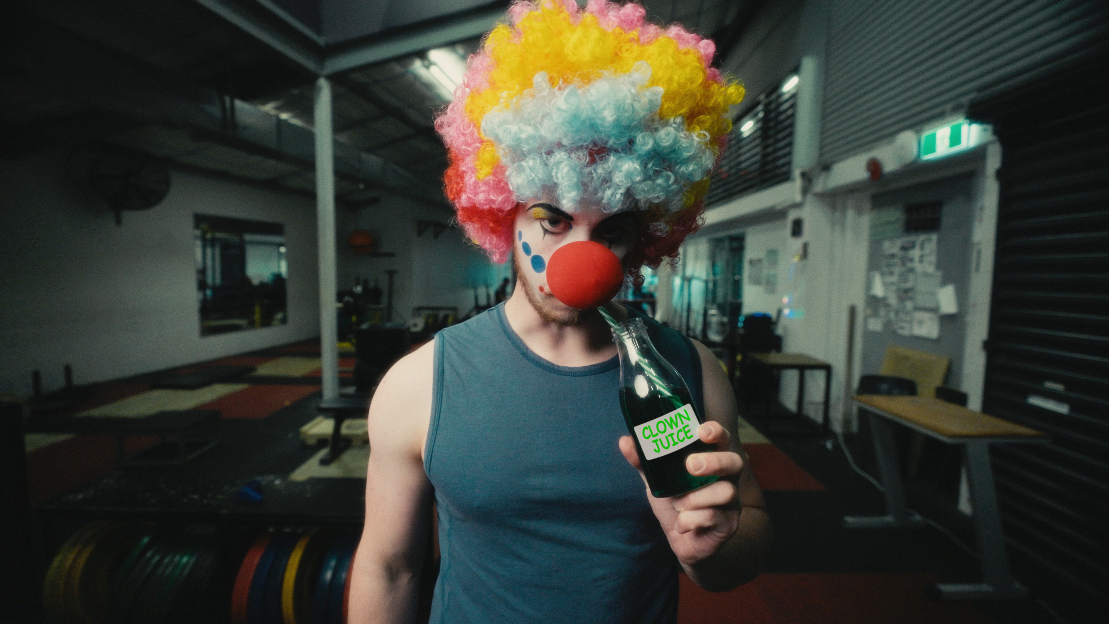 Sinister gym clown drinks from a bottle marked 'Clown Juice'.